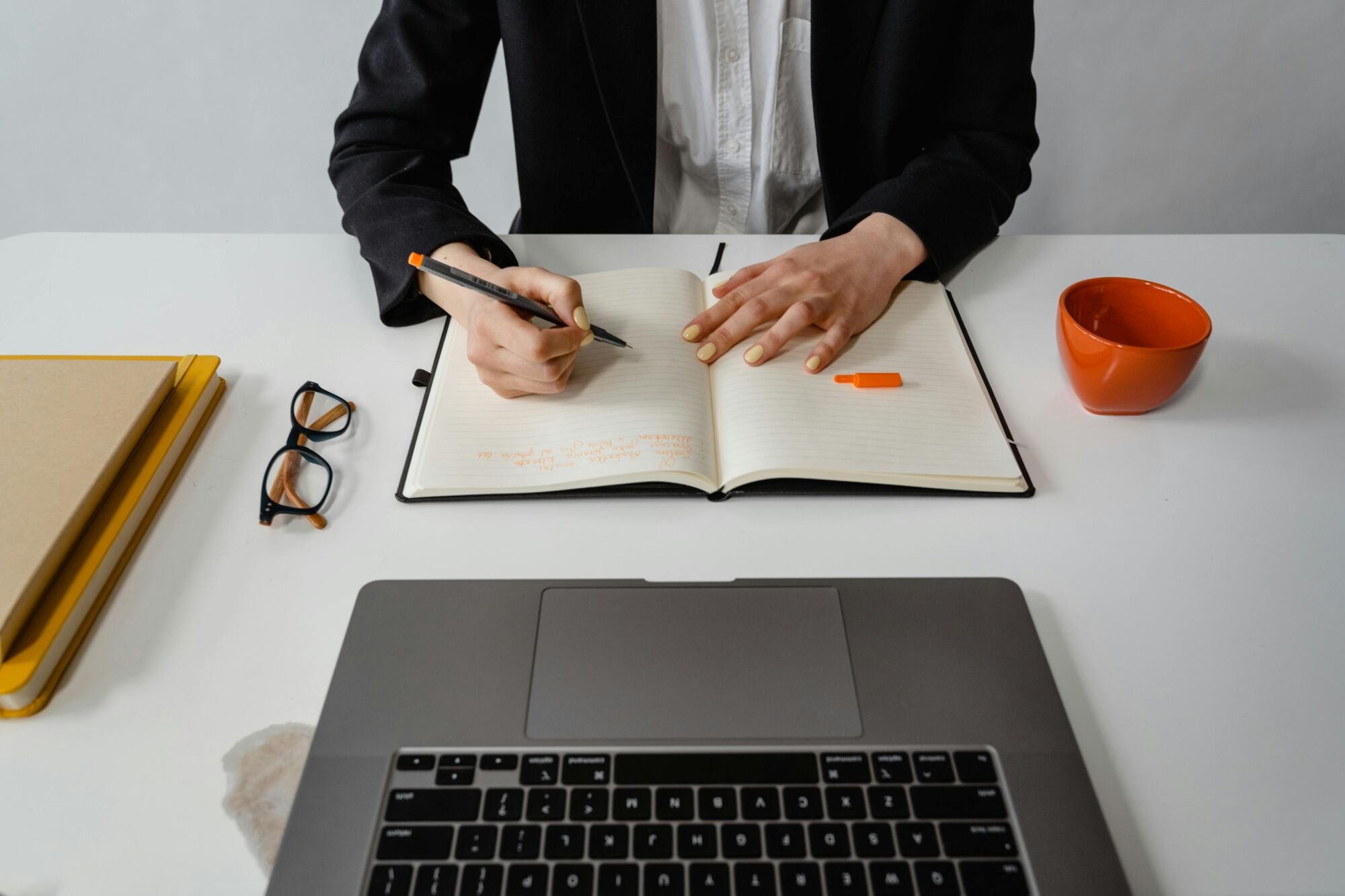 A business professional writes notes during work at a clean, minimalist desk setup with a laptop.